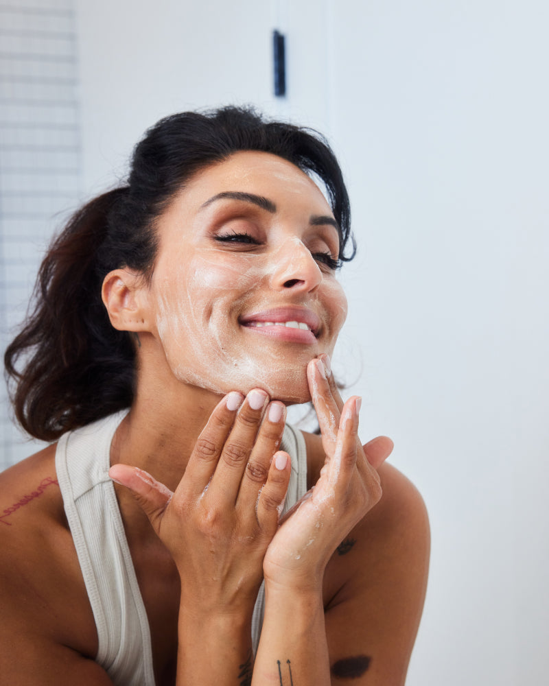 Woman applying Bio-Cleanse 5.5 Face wash lather to her face, smiling with eyes closed gallery position 1
