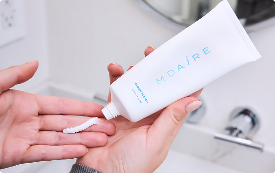 Person dispensing creamy white Cloud Polish from MDAiRE tube onto fingertip in bathroom sink area